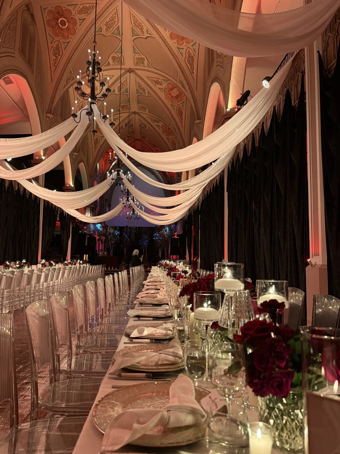 Reception hall set up with white drapes, long candlelit tables and red roses